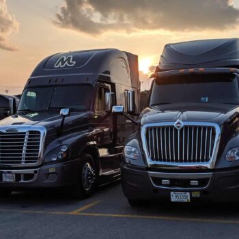 Front view of two Midwest Carriers trucks parked in the lot with the sun setting